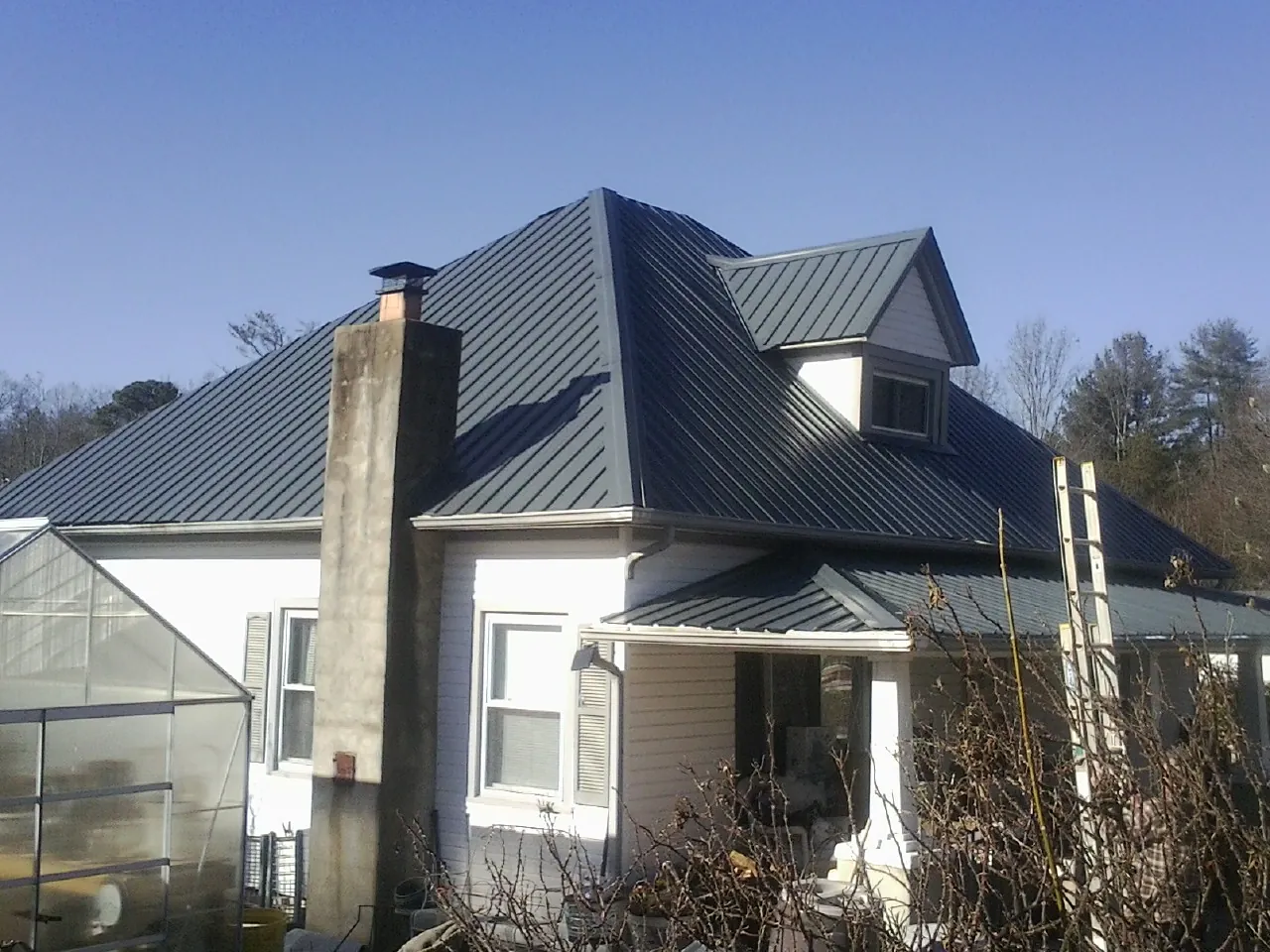 Dark blue standing seam metal roof on a white farmhouse with dormer — Slate & Tile Roof Repair by Roofing Brothers in Linwood