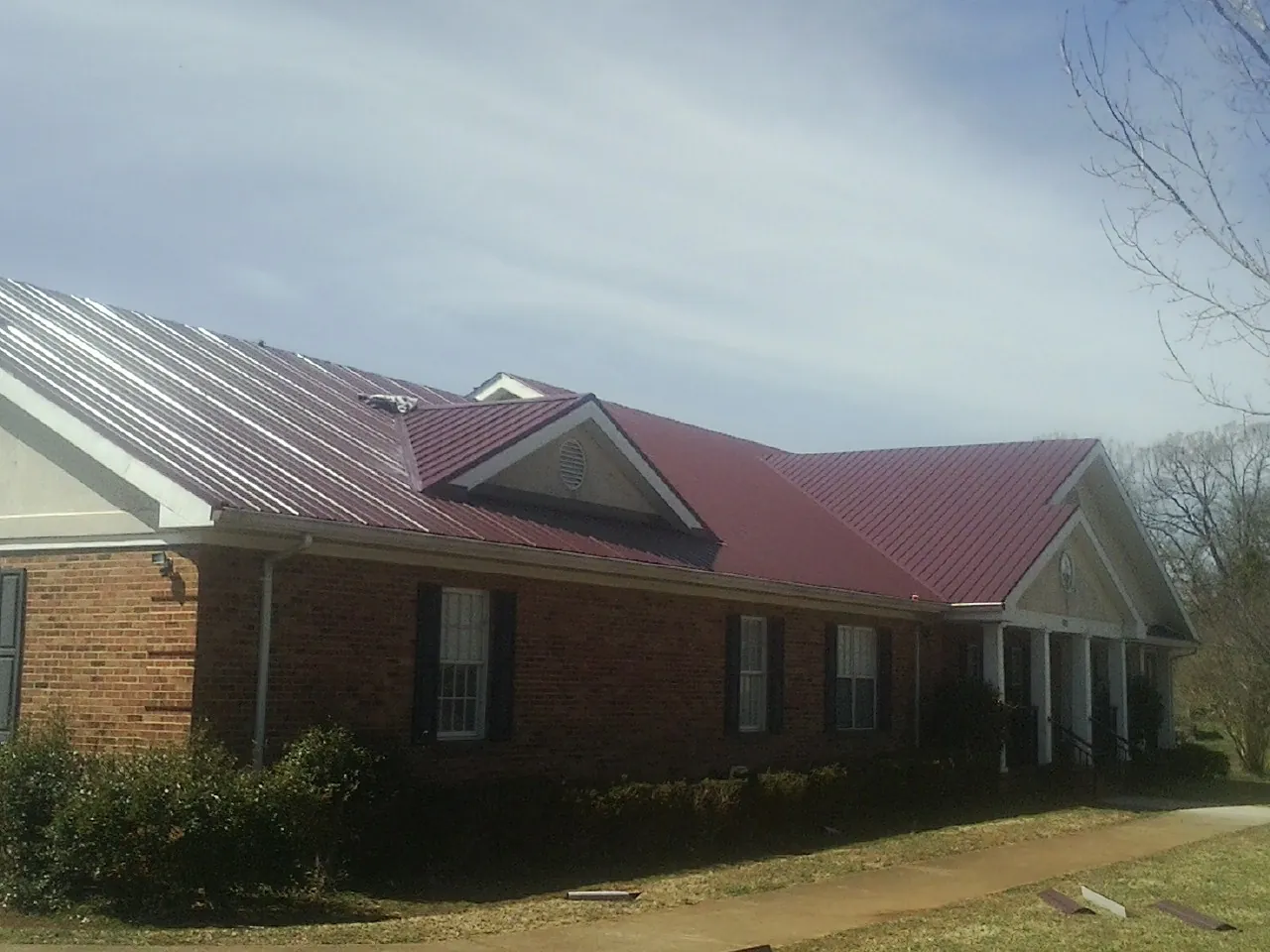 Red metal roof with gabled entries on a long brick building, from a Hail Damage Roof Repair job in Linwood