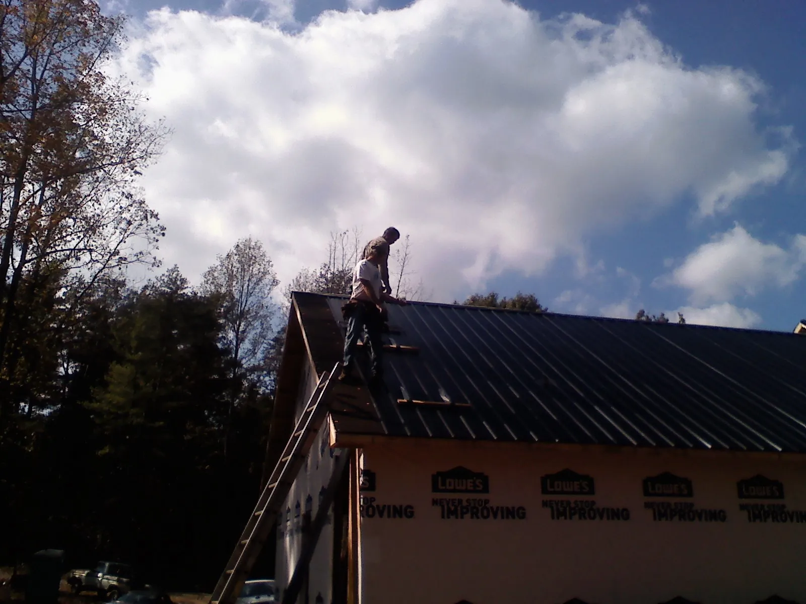 Roofer fastening dark metal panels high against a cloudy sky, from a Roof Inspection job in Linwood